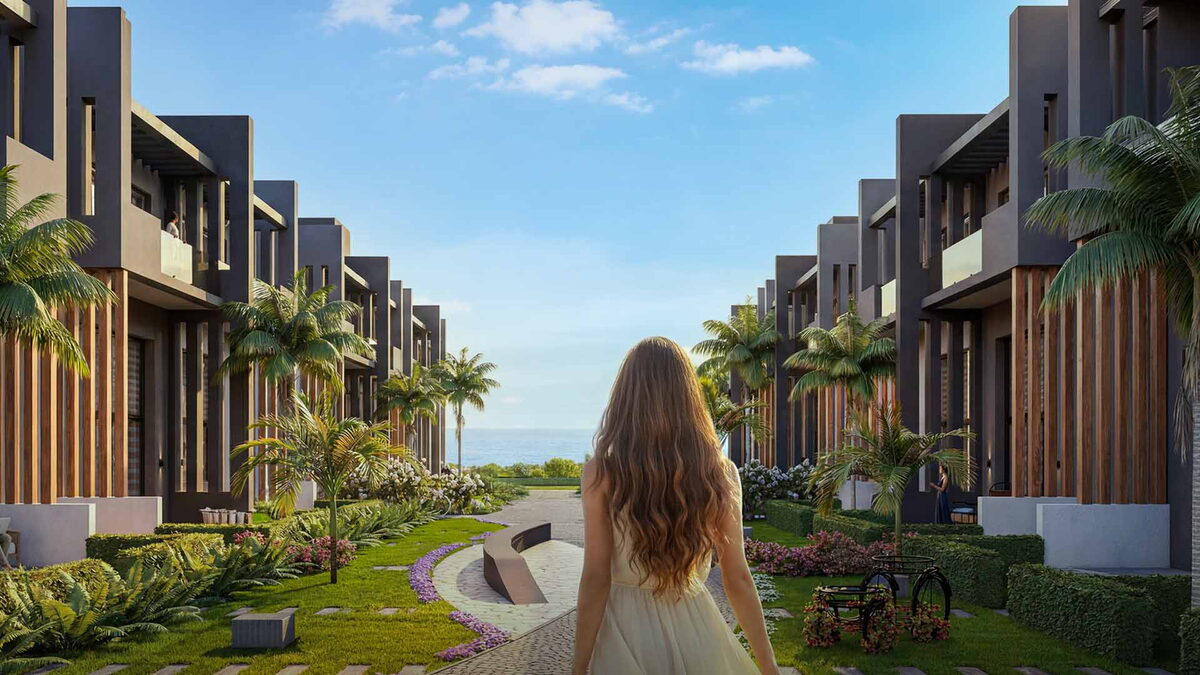 Sky Diora — Villalar arasındaki peyzajlı yolda yürüyen kadın, ufukta deniz görselleştirmesi