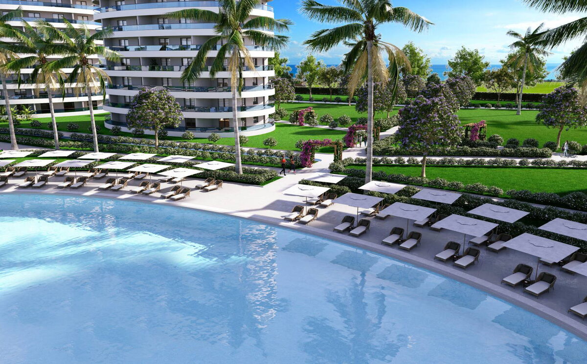 Ocean Life Residence — Geniş yüzme havuzu kenarında şezlong sıraları, arkada bloklar ve deniz (görselleştirme)